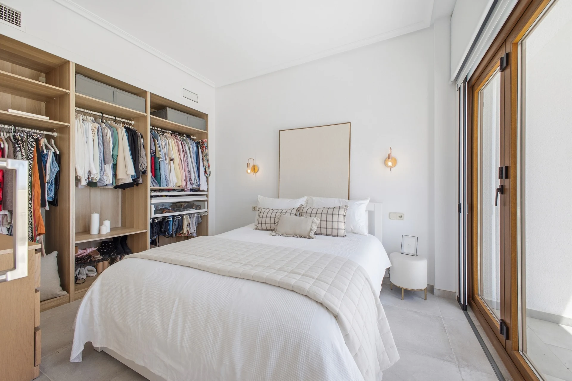 Dormitorio con cama, armarios abiertos y acceso a la terraza