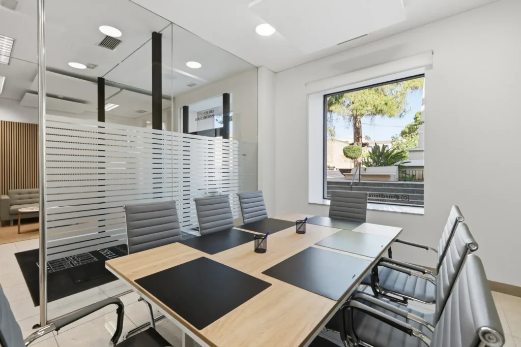 Sala de reuniones con mesa de madera, sillas grises y mamparas de cristal
