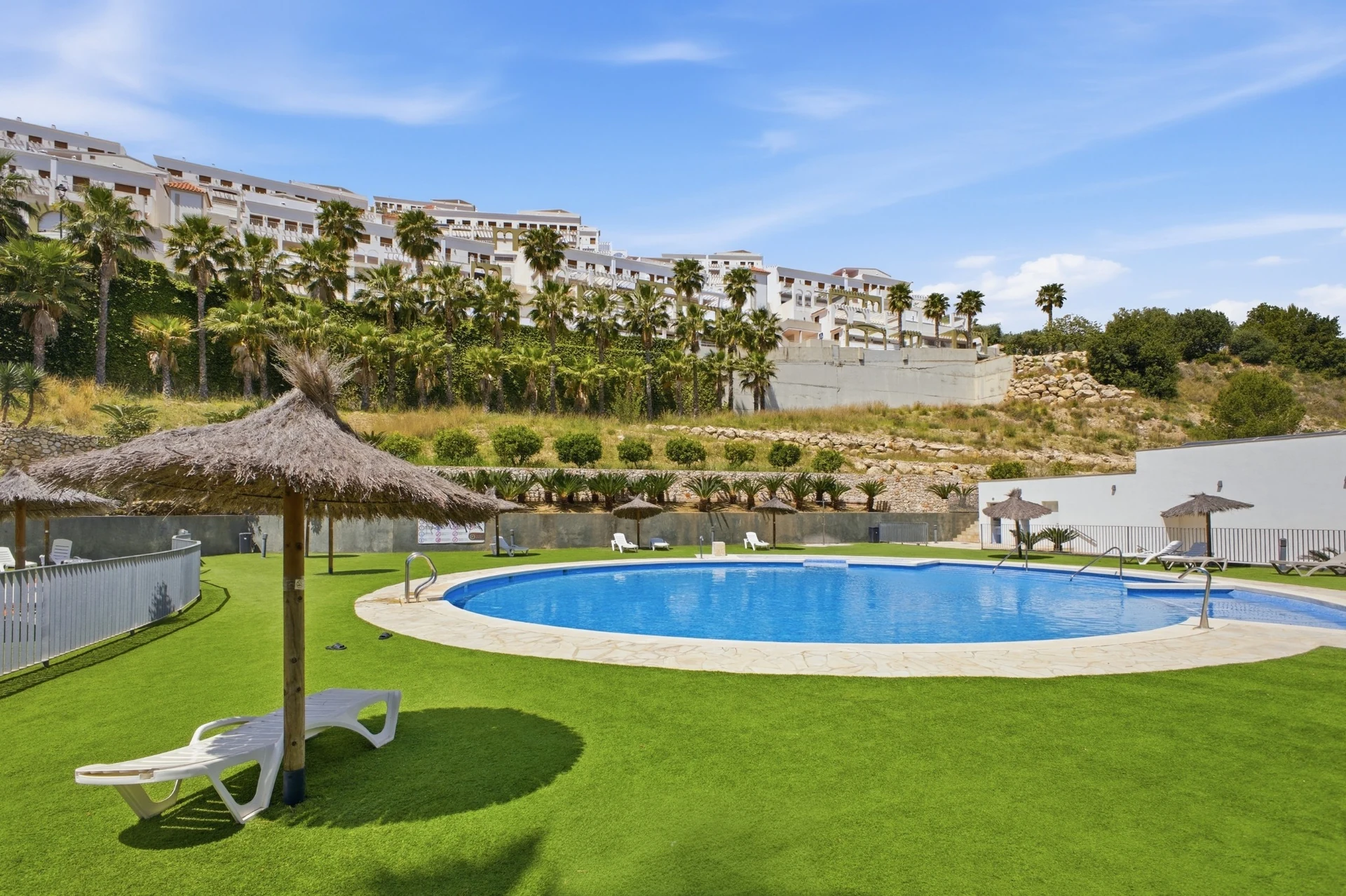 Piscina exterior con jardín y tumbonas en las zonas comunes